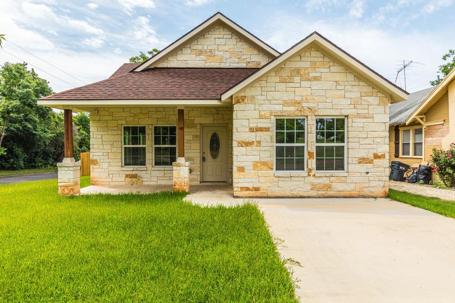 View of front of property featuring a shingled roof, stone siding, and a front lawn