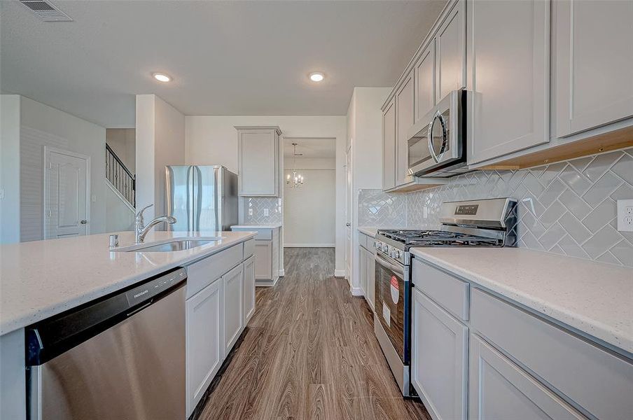 A chef’s kitchen with stainless appliances that feature a 5-burner gas range, microwave & dishwasher.