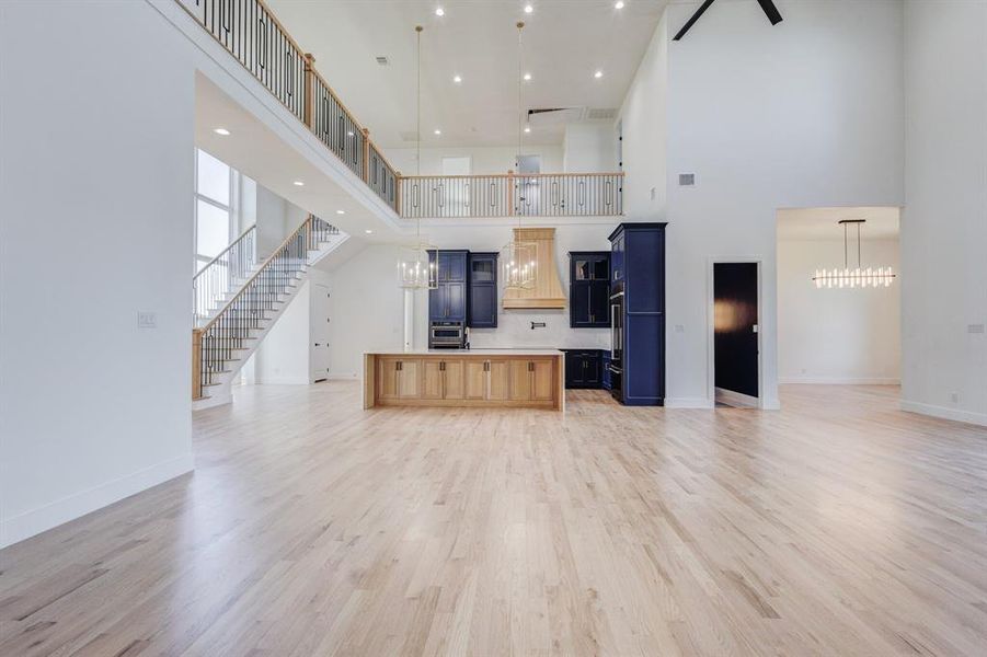 Expansive great room featuring light wood-finish flooring, a two-story ceiling, and a prominent staircase with a wrought iron railing