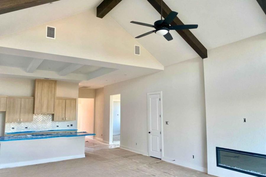 Kitchen featuring beamed ceiling, high vaulted ceiling, decorative backsplash, light brown cabinetry, and a large fireplace