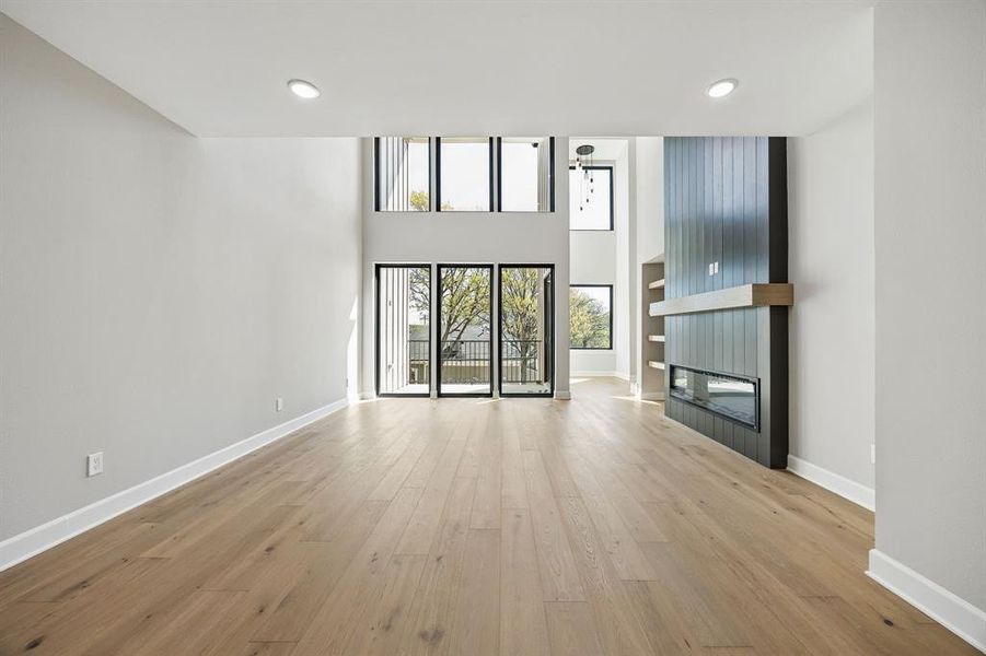 Unfurnished living room with a high ceiling, light wood-style floors, a large fireplace, and recessed lighting Unfurnished living room with a high ceiling, light wood-style floors, a large fireplace, and recessed lighting
