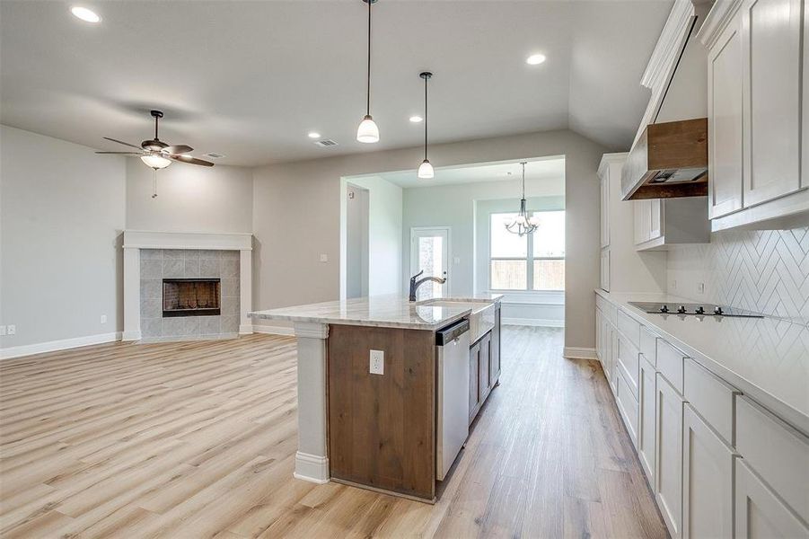 Kitchen with white cabinets, pendant lighting, light hardwood / wood-style floors, a tile fireplace, and an island with sink