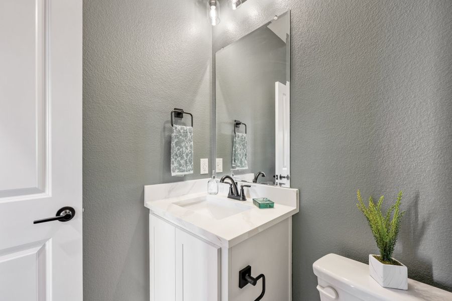 Powder room with white vanity, white quartz countertop, large mirror, and gray textured walls