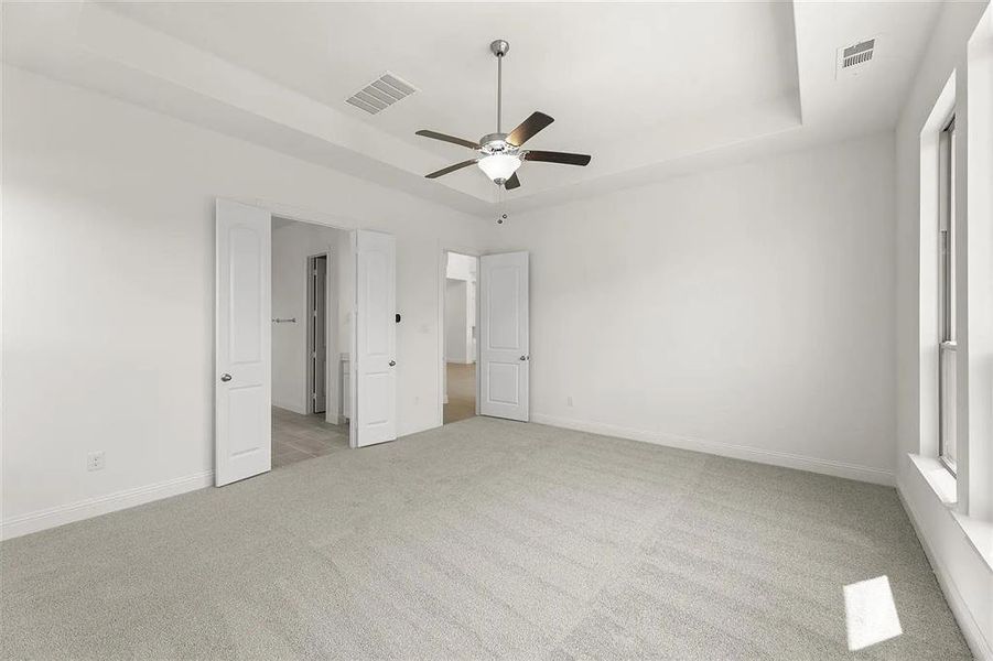 Unfurnished bedroom featuring light colored carpet, a raised ceiling, and ceiling fan