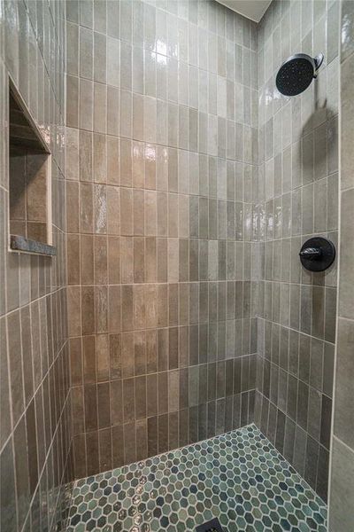 Shower enclosure featuring vertically stacked tile walls in varying shades of gray, a built-in shower niche with a stone sill, and a contrasting hexagonal mosaic tile floor