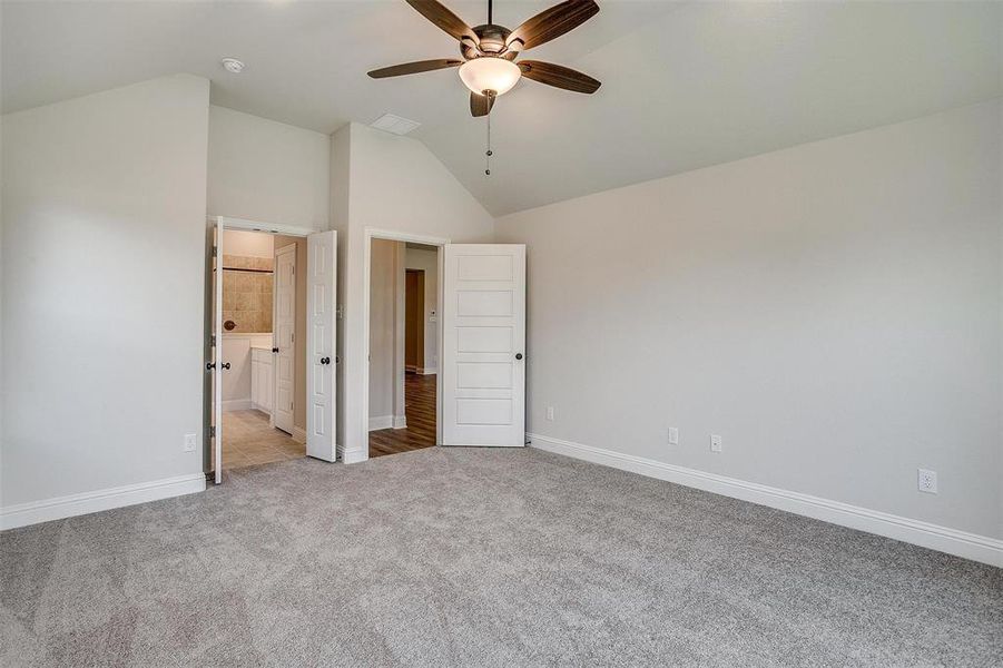 Unfurnished bedroom featuring light colored carpet, ensuite bath, high vaulted ceiling, and ceiling fan