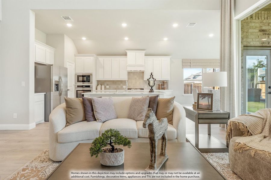 Open-concept living room with cream sofa and kitchen featuring white cabinets and stainless steel appliances in background Open-concept living room with cream sofa and kitchen featuring white cabinets and stainless steel appliances in background