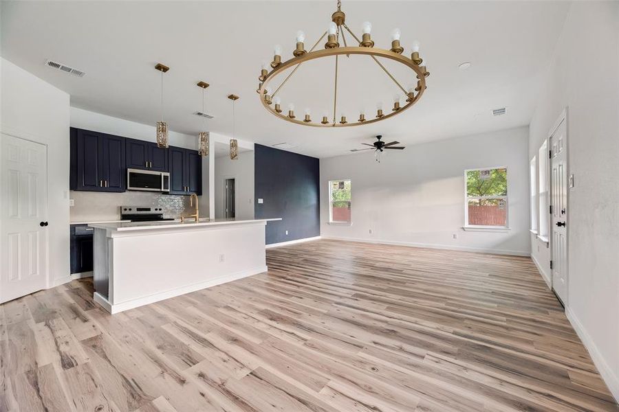Kitchen featuring open floor plan, suspended lighting, light countertops, a kitchen island with sink, and stainless steel microwave