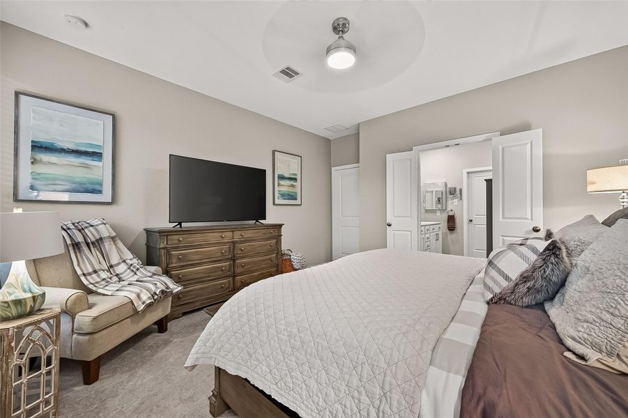Spacious primary bedroom featuring neutral finishes, plush carpeting, a ceiling fan, and ample room for a full furniture suite. Double doors provide convenient access to the private en-suite bath, creating a comfortable and functional retreat. Spacious primary bedroom featuring neutral finishes, plush carpeting, a ceiling fan, and ample room for a full furniture suite. Double doors provide convenient access to the private en-suite bath, creating a comfortable and functional retreat.
