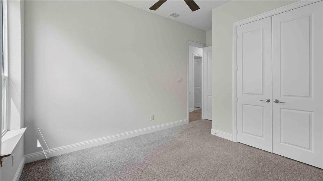 Light-colored wall paint and carpeting, dual panel doors, single window, and ceiling fan