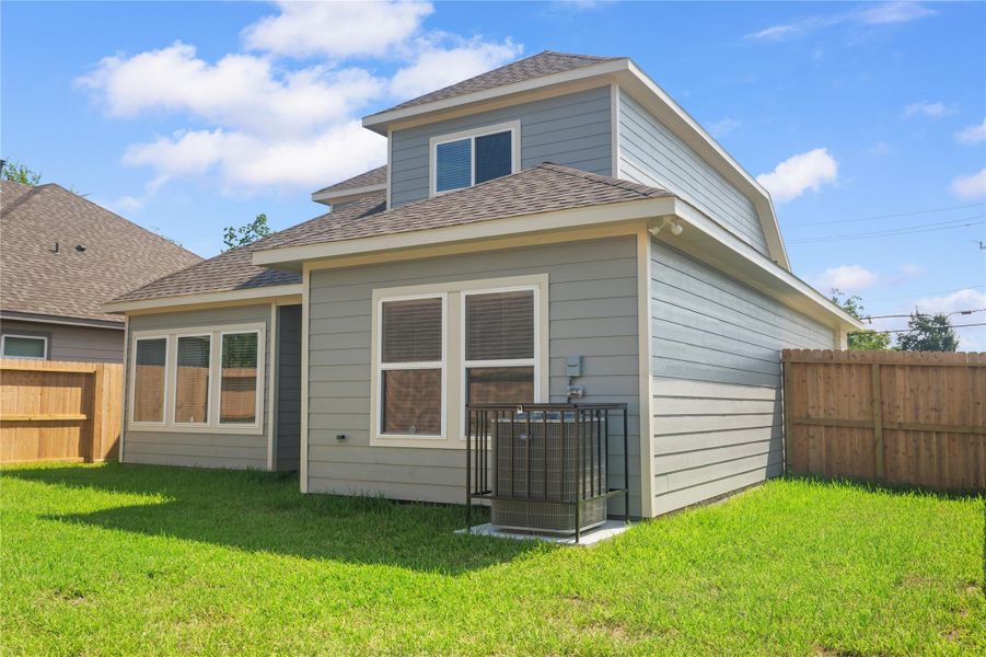 This photo shows the back of a modern two-story home with gray siding, large windows, and a fenced backyard featuring a well-maintained lawn.