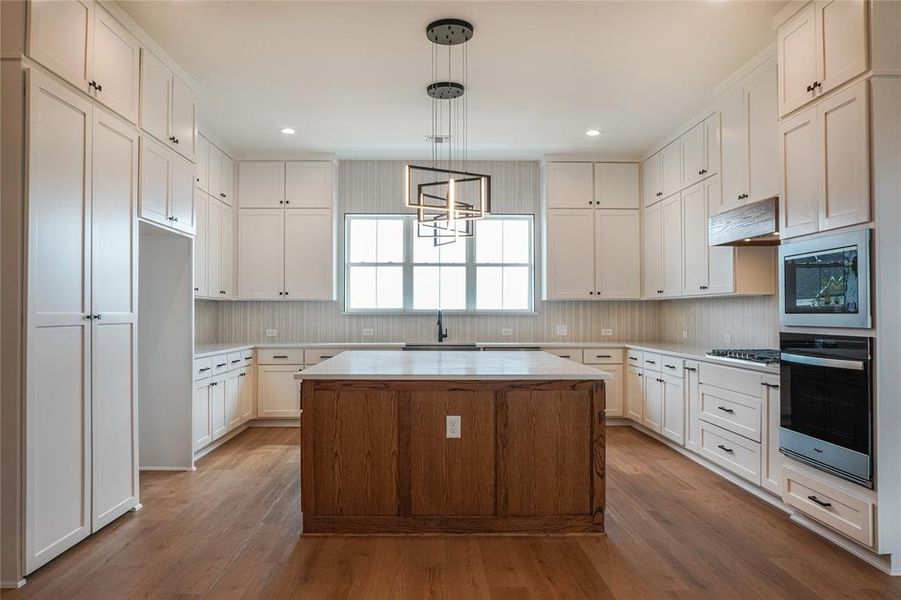 Kitchen featuring light wood-type flooring, a center island, white cabinets, and stainless steel appliances