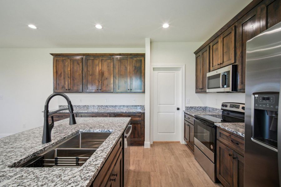 Kitchen featuring a sink, light stone counters, light wood-style flooring, dark brown cabinetry, and appliances with stainless steel finishes Kitchen featuring a sink, light stone counters, light wood-style flooring, dark brown cabinetry, and appliances with stainless steel finishes