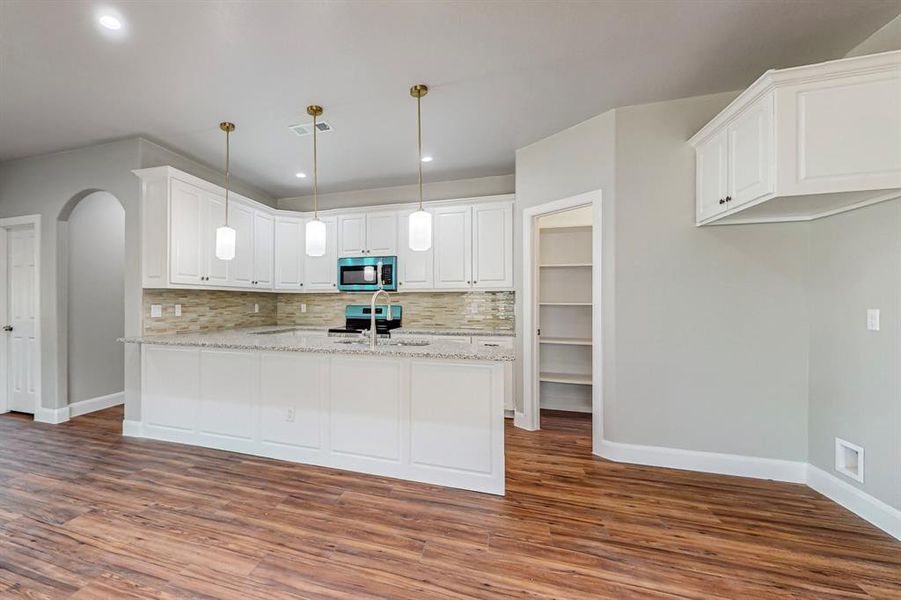 Kitchen with backsplash, hardwood / wood-style flooring, white cabinetry, and hanging light fixtures