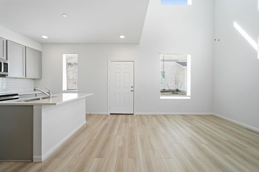 Kitchen featuring gray cabinets, light wood-style flooring, light stone countertops, backsplash, and stainless steel microwave