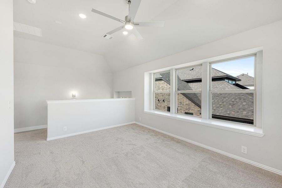 Empty bedroom with vaulted ceiling, ceiling fan, carpet flooring, and large triple window
