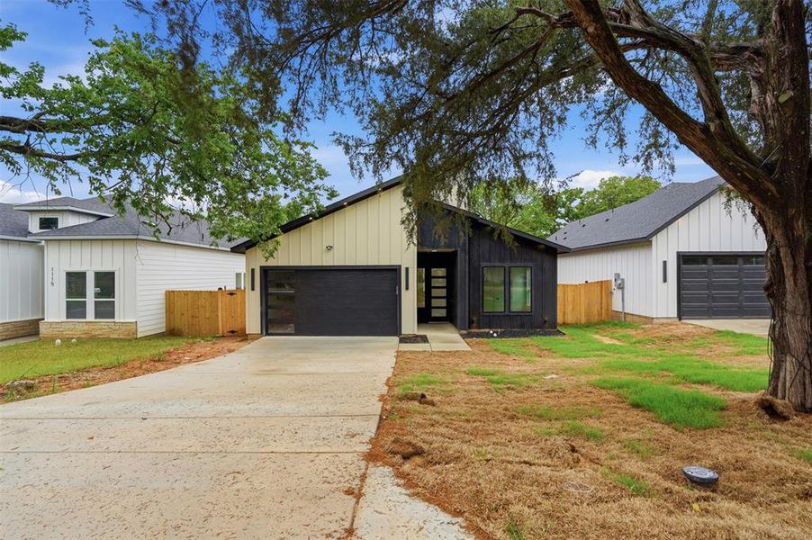 Contemporary exterior featuring a black and cream-colored facade, an attached garage with a dark sectional door, a concrete driveway, and a modern entry door with frosted glass panels