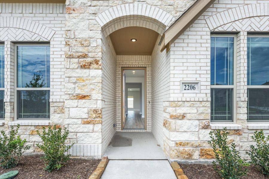 Front entry of home with arched stone surround, open door, and house number 2206 on white brick exterior.