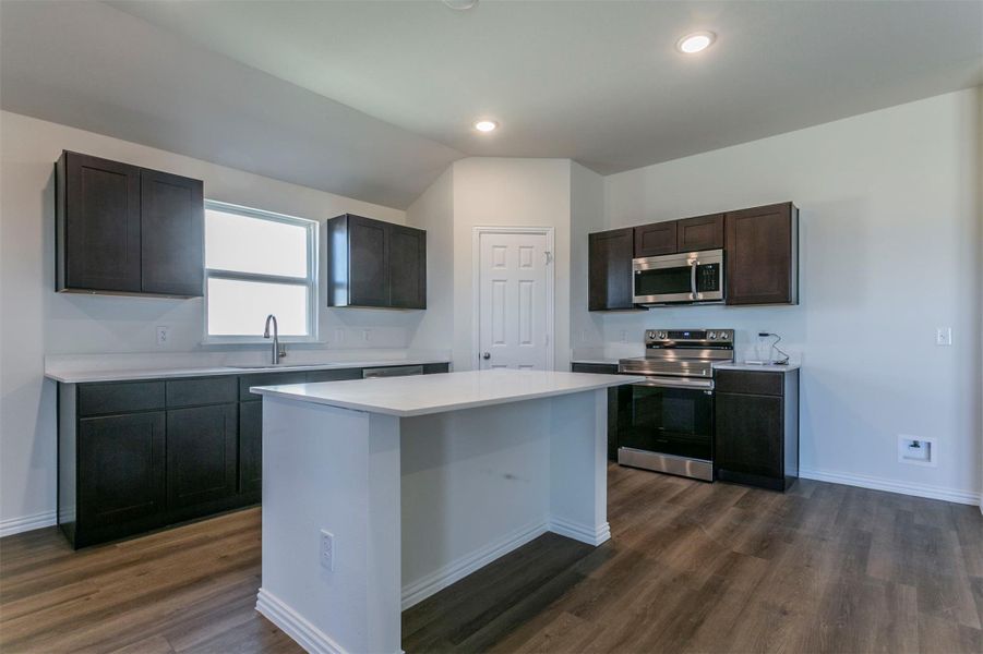 Kitchen with stainless steel appliances, a center island, a sink, dark wood-style flooring, and light countertops Kitchen with stainless steel appliances, a center island, a sink, dark wood-style flooring, and light countertops