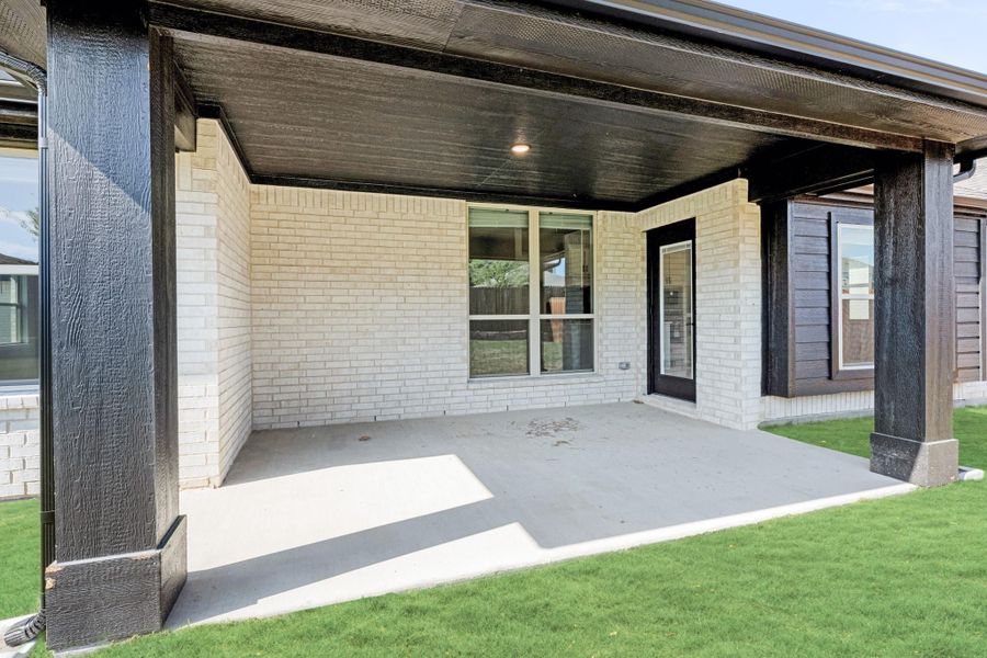 Covered back patio with concrete floor, dark wood columns, and brick exterior walls adjacent to green lawn Covered back patio with concrete floor, dark wood columns, and brick exterior walls adjacent to green lawn