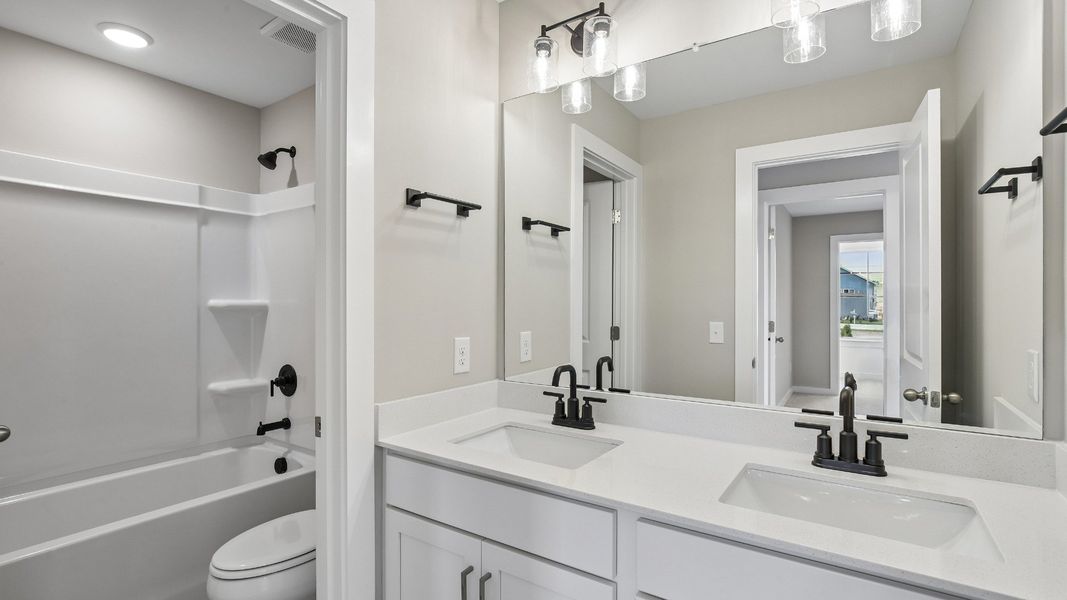Secondary bathroom with dual vanity and door to shower and toilet