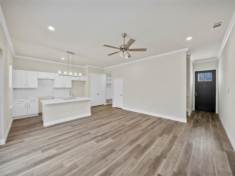Unfurnished living room featuring light wood-style floors, visible vents, a sink, and baseboards