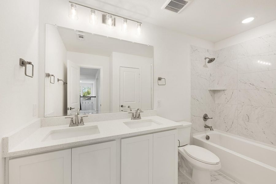 Bathroom with double sink vanity, white cabinets, quartz countertop, and tub-shower with marble tile surround
