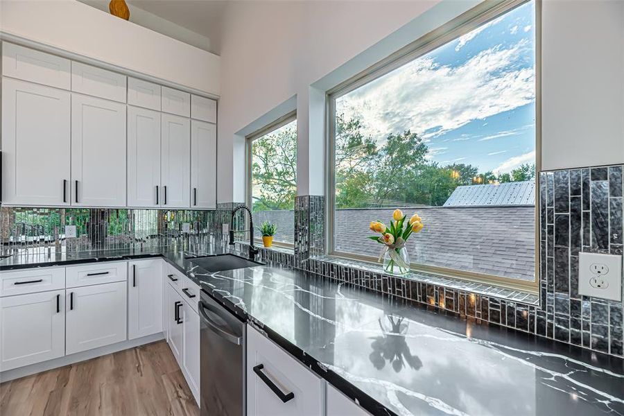 Modern kitchen featuring white cabinetry, glossy dark countertops, and a large window with a serene view, bringing in plenty of natural light.