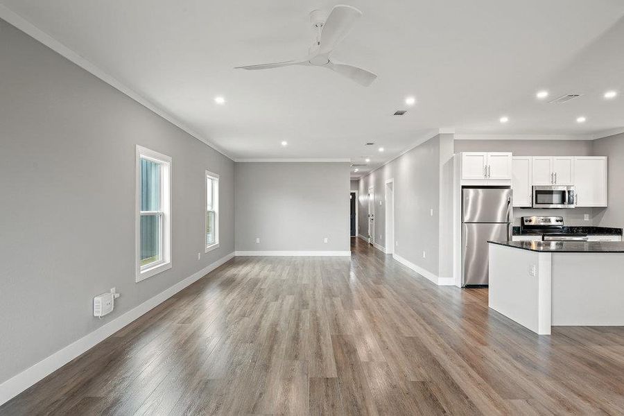 Kitchen with open floor plan, appliances with stainless steel finishes, white cabinetry, crown molding, and light wood-style flooring