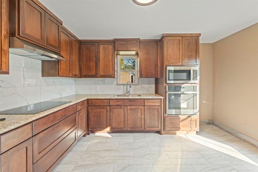 Kitchen featuring light marble finish flooring, decorative backsplash, stainless steel appliances, and light stone countertops Kitchen featuring light marble finish flooring, decorative backsplash, stainless steel appliances, and light stone countertops