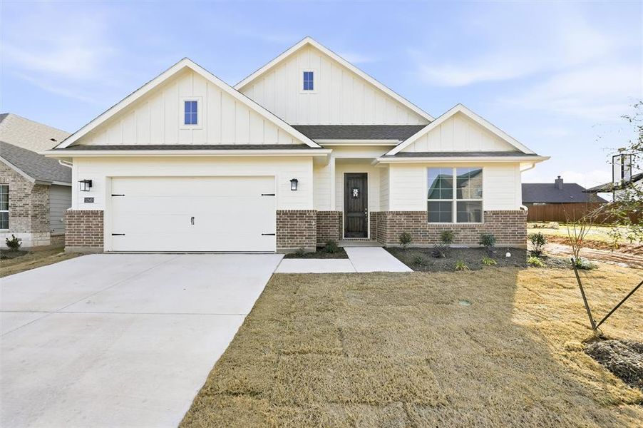View of front of home featuring board and batten siding, brick siding, driveway, a front yard, and a shingled roof