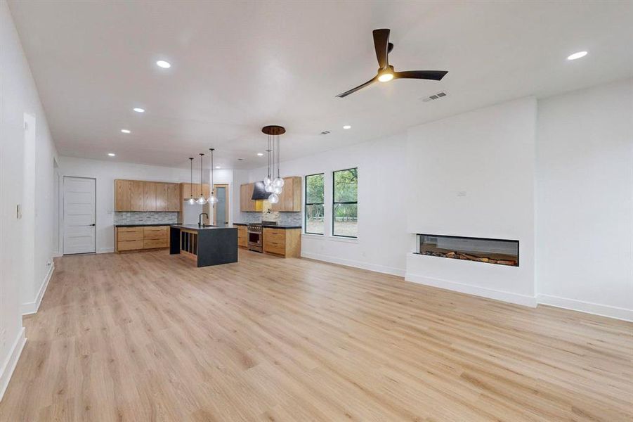 Spacious open-concept living area featuring wood-finish flooring, recessed lighting, and a modern linear fireplace Spacious open-concept living area featuring wood-finish flooring, recessed lighting, and a modern linear fireplace