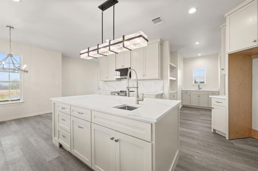 Kitchen featuring a kitchen island with sink, decorative backsplash, hanging light fixtures, white cabinetry, and wood finished floors Kitchen featuring a kitchen island with sink, decorative backsplash, hanging light fixtures, white cabinetry, and wood finished floors