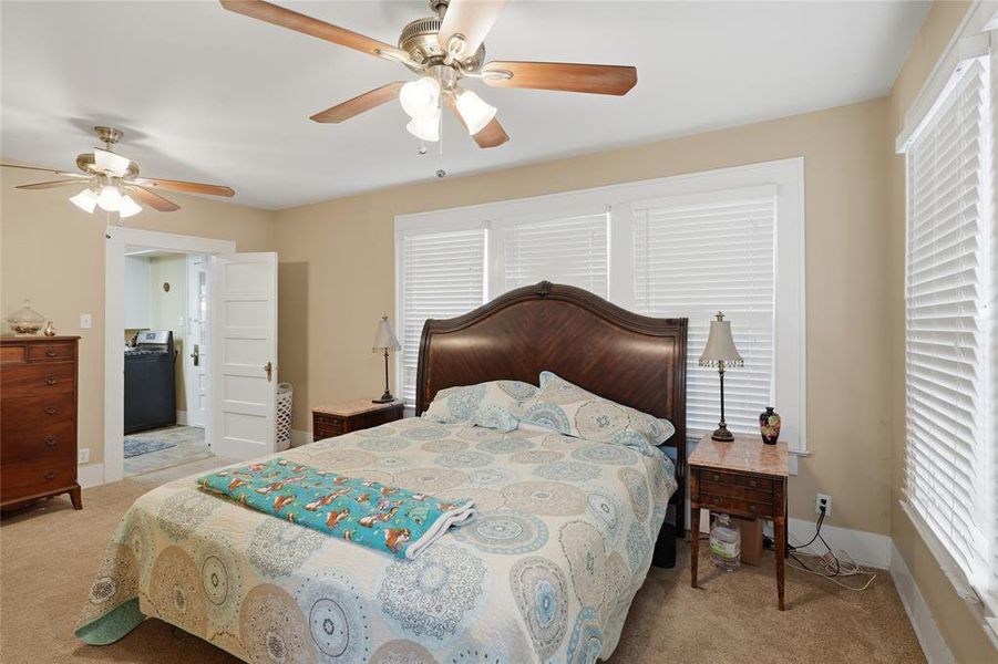 Carpeted room featuring a dark wood headboard, multiple windows with blinds, and two ceiling fans with integrated lighting