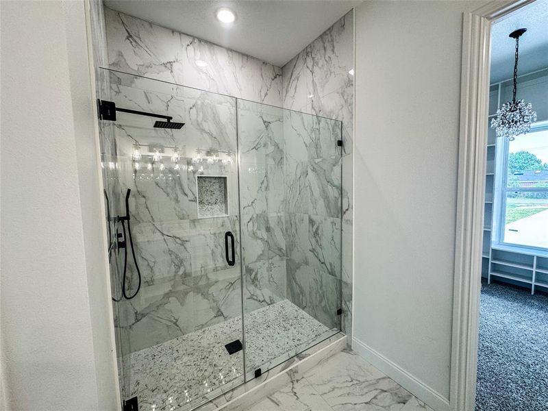 Full bath with a marble finish shower, baseboards, a chandelier, and marble look tile flooring Full bath with a marble finish shower, baseboards, a chandelier, and marble look tile flooring
