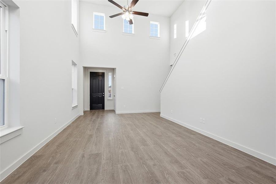 Double-height living space featuring wood-finish flooring, a contemporary ceiling fan, and multiple windows Double-height living space featuring wood-finish flooring, a contemporary ceiling fan, and multiple windows