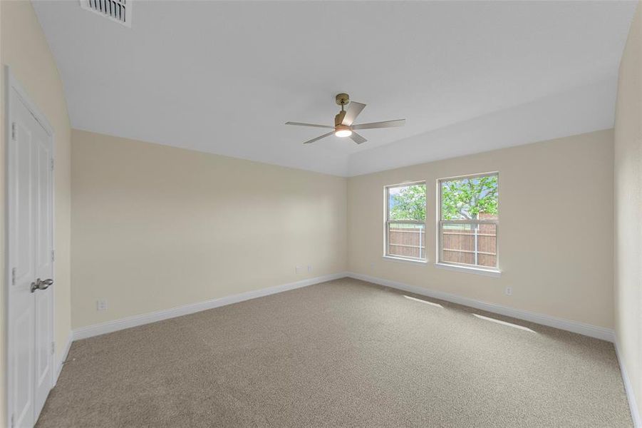 Spacious interior room featuring a tray ceiling, two windows, carpet flooring, and a ceiling fan with integrated lighting