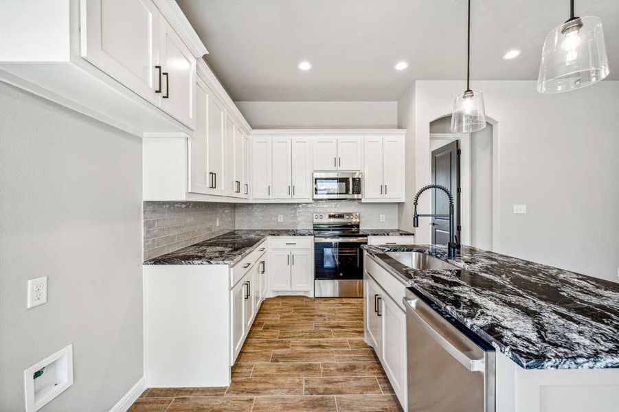 Kitchen featuring pendant lighting, stainless steel appliances, white cabinetry, and tasteful backsplash