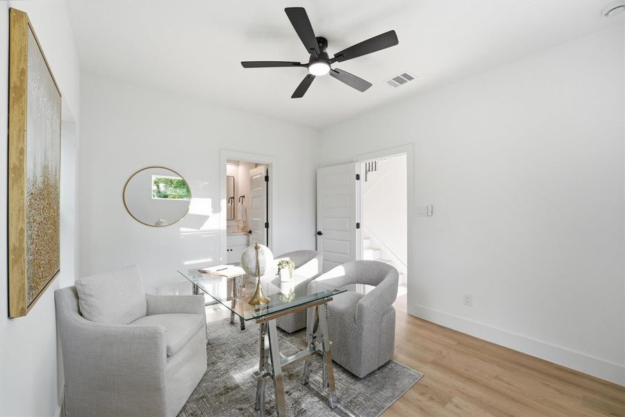 Bright, stylish flex room ideal as a home office or study, featuring wood-look flooring, modern ceiling fan, clean white walls, and natural light flowing in from multiple windows.