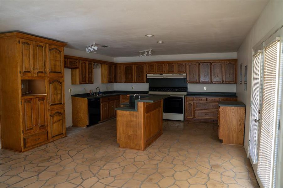 Kitchen featuring dark countertops, black appliances, a kitchen island with sink, and brown cabinets