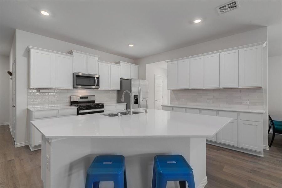 Kitchen with visible vents, dark wood-style flooring, a kitchen island with sink, stainless steel appliances, and a sink