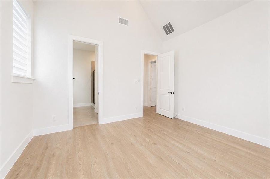Room featuring vaulted ceilings, light wood-finish flooring, white walls, and a window with horizontal blinds