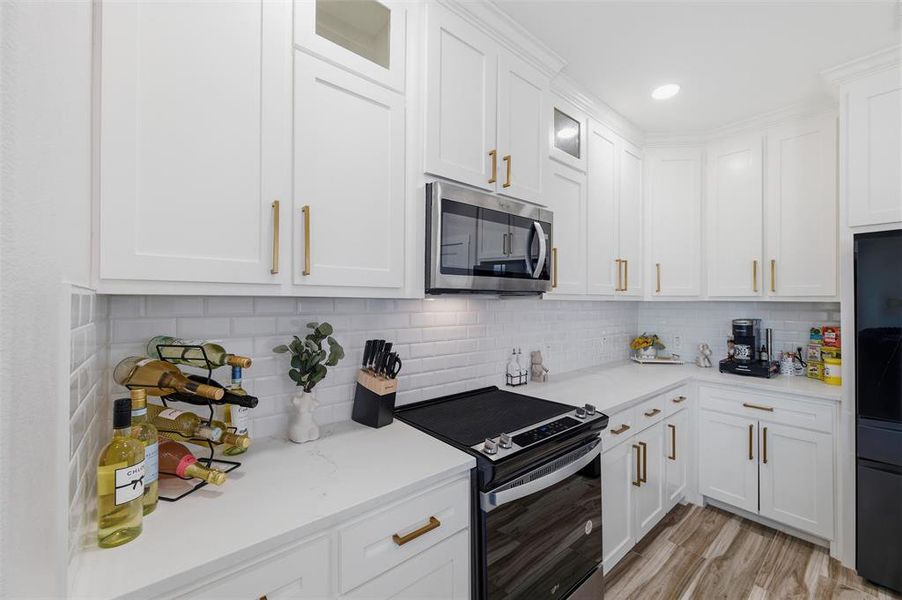 Kitchen featuring stainless steel appliances, glass insert cabinets, white cabinetry, decorative backsplash, and recessed lighting