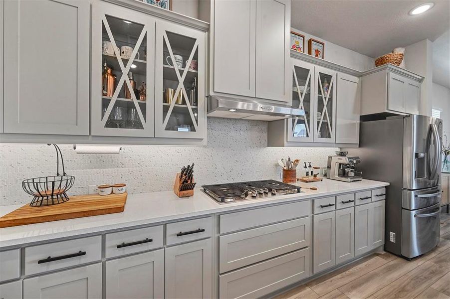 Kitchen with under cabinet range hood, stainless steel appliances, light wood-style flooring, tasteful backsplash, and light countertops Kitchen with under cabinet range hood, stainless steel appliances, light wood-style flooring, tasteful backsplash, and light countertops