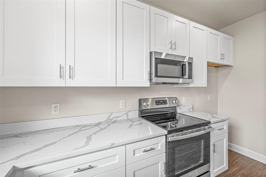 Kitchen with stainless steel appliances, dark wood-type flooring, white cabinets, and light stone counters