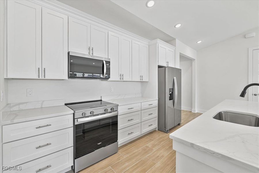 Kitchen with appliances with stainless steel finishes, light stone counters, white cabinets, wood tiled floors, and recessed lighting