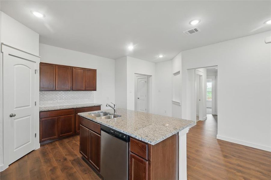 Kitchen with dishwasher, dark wood-style flooring, light stone countertops, a kitchen island with sink, and tasteful backsplash Kitchen with dishwasher, dark wood-style flooring, light stone countertops, a kitchen island with sink, and tasteful backsplash