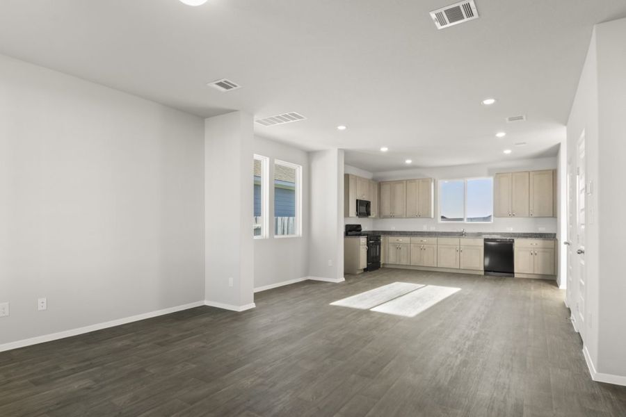 Image of a living room with dark vinyl flooring, light grey walls, and a open kitchen in the distance
