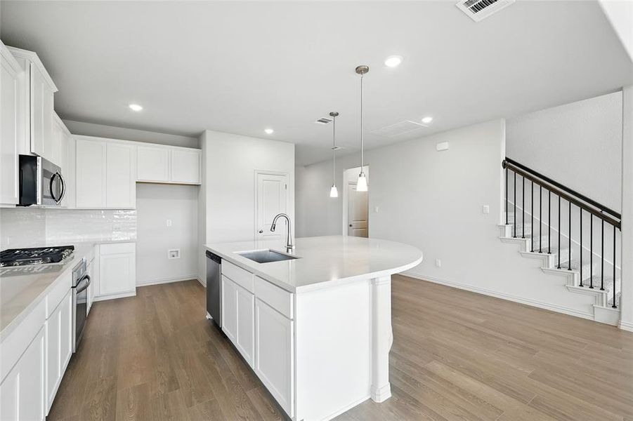 Kitchen with white cabinets, an island with sink, decorative backsplash, decorative light fixtures, and recessed lighting