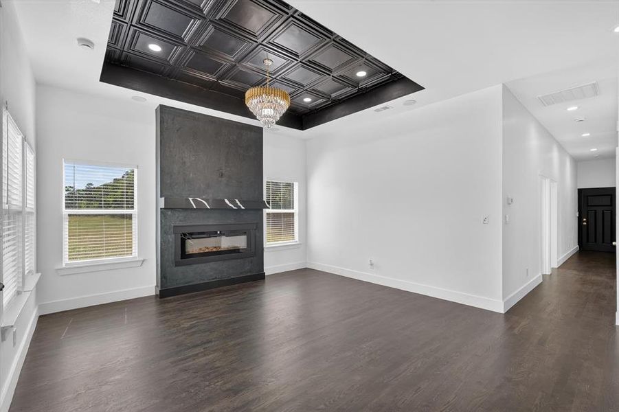 Spacious living area featuring a modern fireplace with a dark surround, a coffered ceiling with recessed lighting, an elegant chandelier, and wood-finish flooring